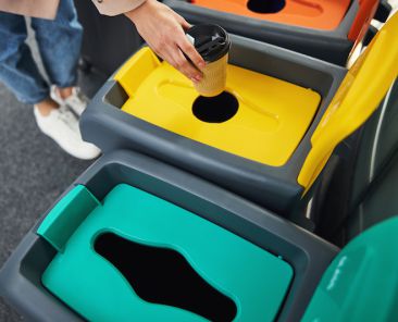 Close up of young woman putting disposable paper cup into recycling garbage container or dustbin
